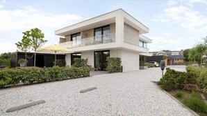 Una casa moderna de dos pisos con balcón, camino de entrada de grava y un pequeño jardín.