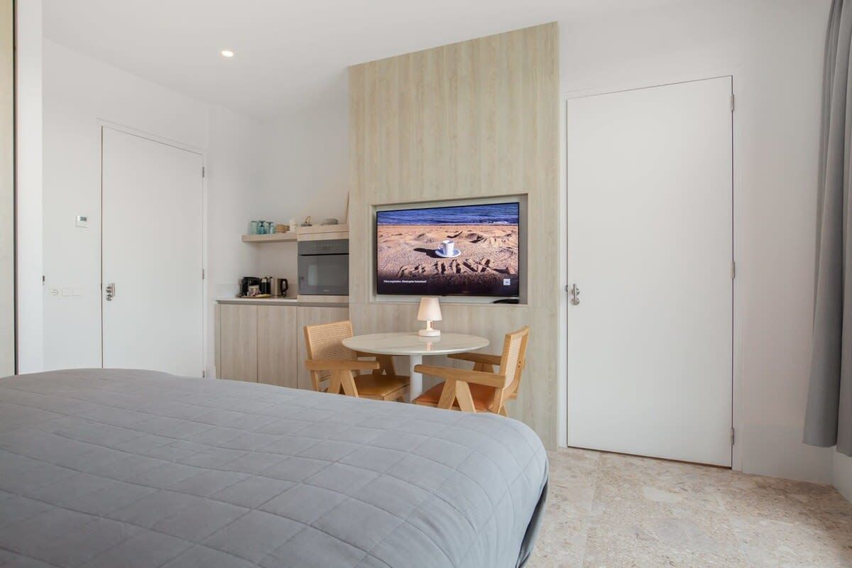 Een slaapkamer met een bed, een eettafel met stoelen, een aan de muur bevestigde televisie en een keuken in de achtergrond.