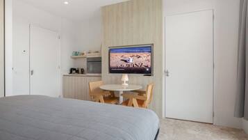 Een slaapkamer met een bed, een eettafel met stoelen, een aan de muur bevestigde televisie en een keuken in de achtergrond.