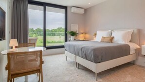 Un dormitorio moderno con una cama grande, un escritorio y una silla. Se ve vegetación por la ventana.