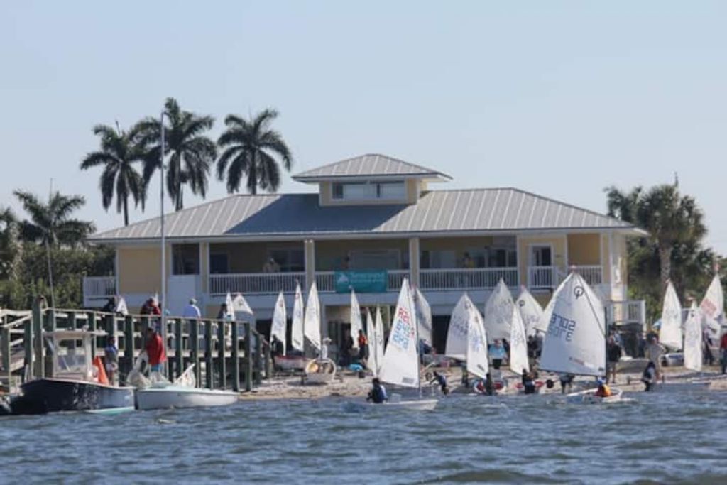 A beachside building with multiple balconies and a dock area with sailboats.