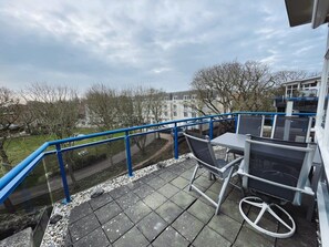 A balcony with a blue railing, a table, and two chairs.