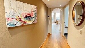 A hallway with a wooden floor, a large abstract painting on the left wall, and a round mirror on the right. - Penthouse near the beach in Domburg | Park Loverendale 31 (Domburg)