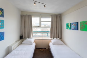 Una habitación con dos camas individuales, una ventana con cortinas y obras de arte en las paredes.