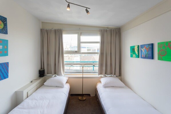 A room with two single beds, a window with curtains, and artwork on the walls.