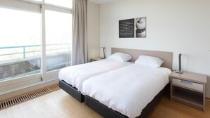 A modern bedroom with a large bed, two bedside tables, and a window with a view. - Penthouse near the beach in Domburg | Park Loverendale 31 (Domburg)