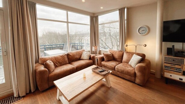 A modern living room with a sectional sofa, a wooden coffee table, and a television on a stand. - Penthouse near the beach in Domburg | Park Loverendale 31 (Domburg)