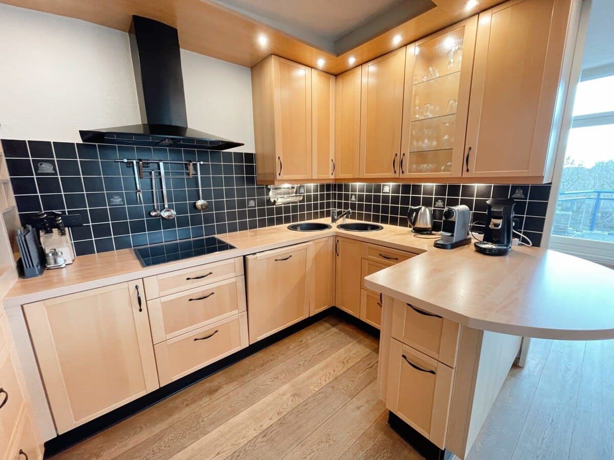 Een moderne keuken met houten kastjes, een zwart betegelde achterwand en een ingebouwde kookplaat.