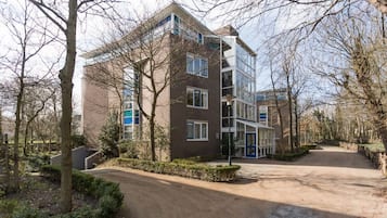 A multi-story residential building with a paved driveway and surrounding trees.