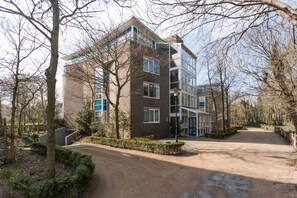 Un edificio residencial de varios pisos con entrada pavimentada y árboles circundantes.