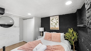 Um quarto moderno com uma cama, uma mesa de cabeceira com abajur, um espelho e uma parede texturizada preta.