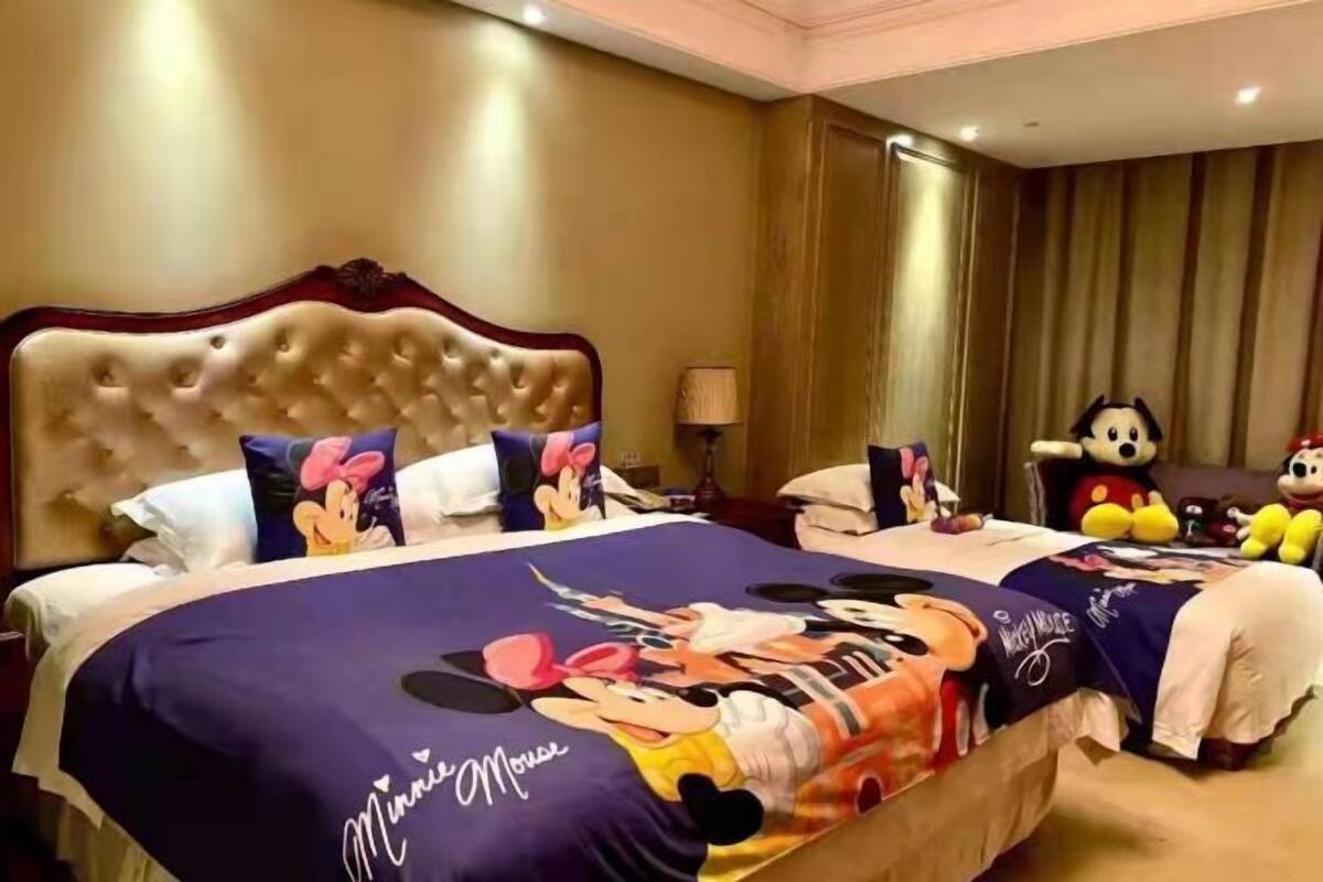 Habitación de hotel con una cama grande, ropa de cama con temática de Minnie Mouse, un cabecero capitonado y una estatua de Mickey Mouse.