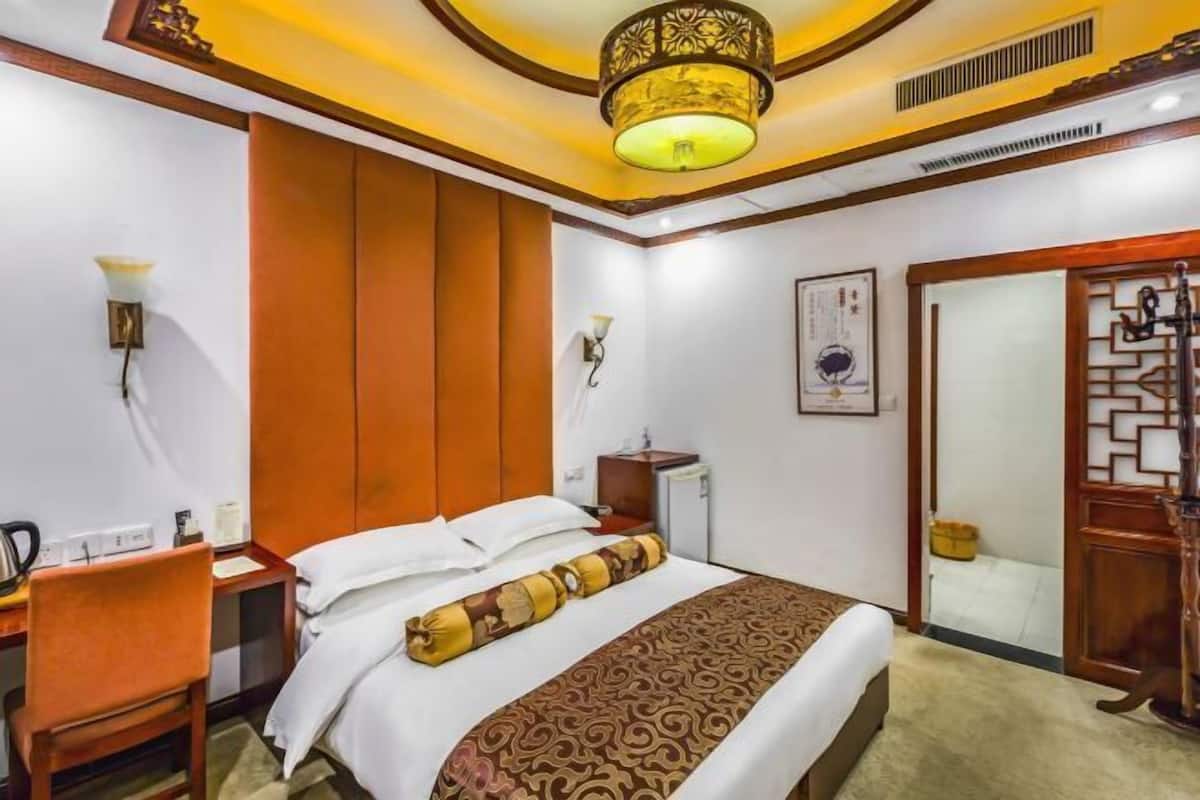 Una habitación de hotel con una cama, un escritorio, una silla, una mesita de noche y una lámpara en la pared.