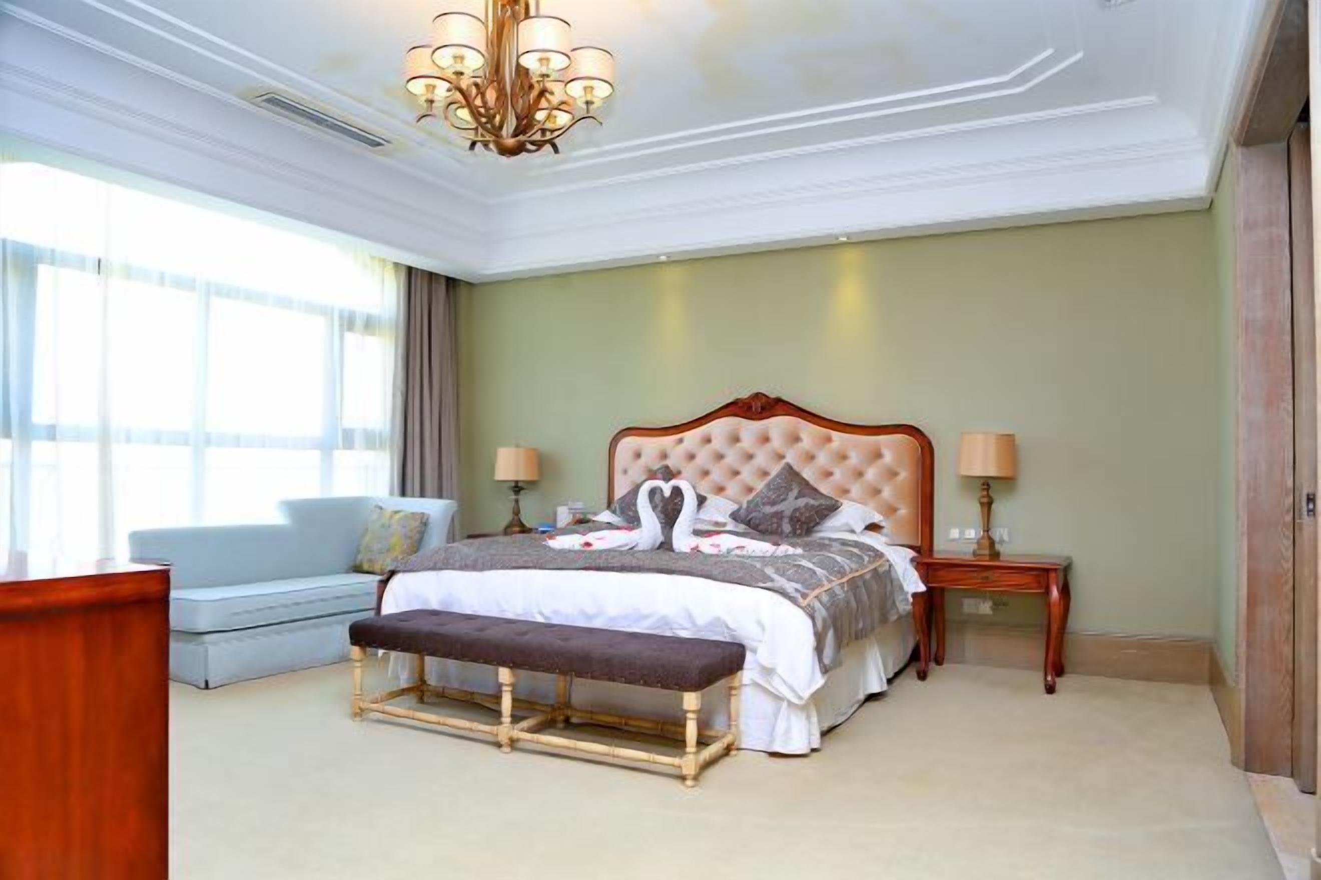 A bedroom with a large bed, a bench, a nightstand, a lamp, and a sofa.