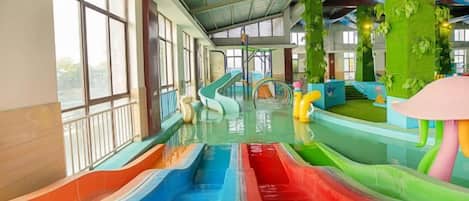 Parque acuático interior con múltiples toboganes y un paisaje artificial verde.