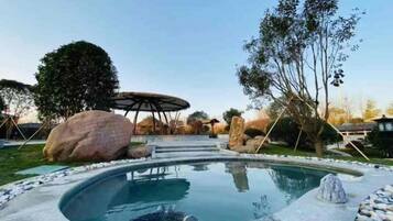 A swimming pool with a hot tub, surrounded by rocks and trees, and a covered seating area in the background.
