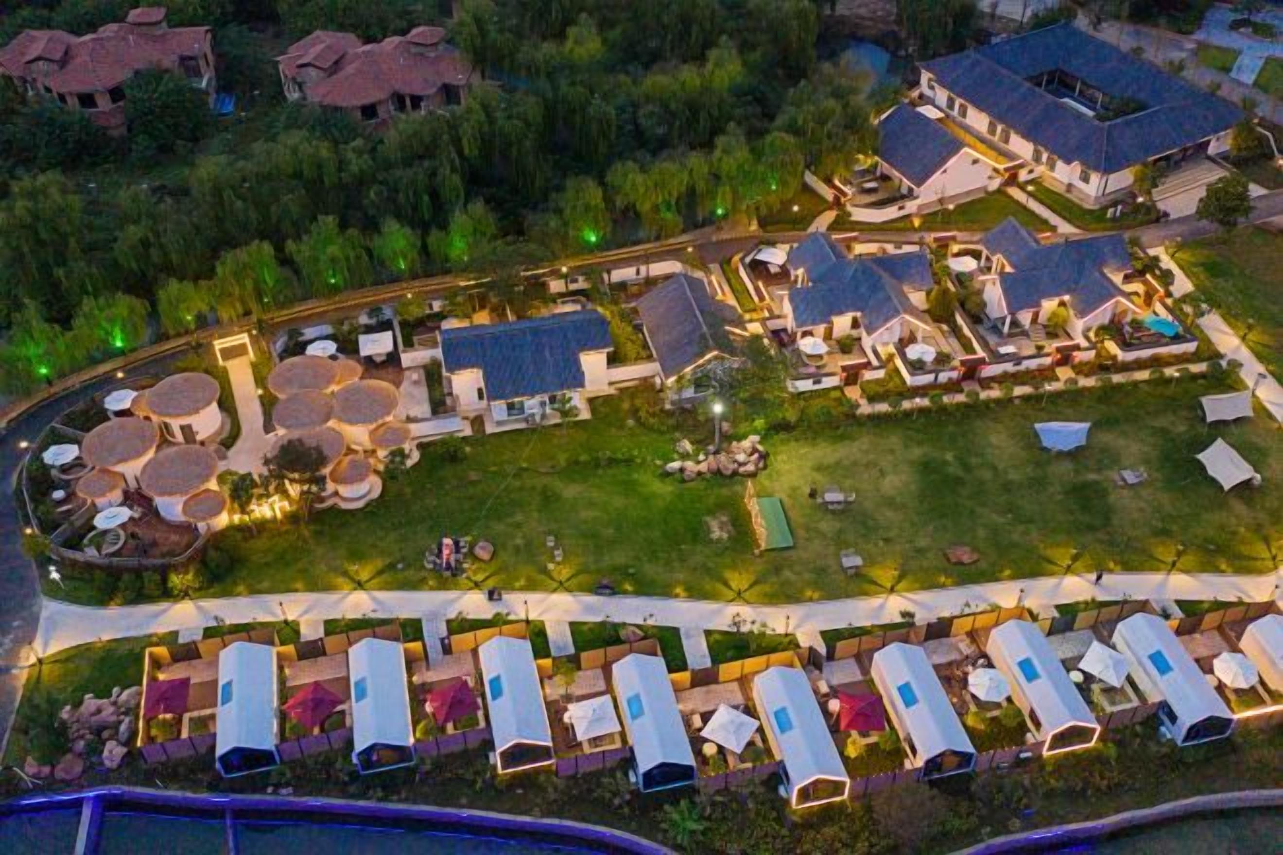 A campground with RVs and tents, a central grassy area, and buildings with pitched roofs.