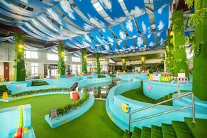Una piscina interior con una decoración azul y verde, rodeada de césped artificial y plantas.