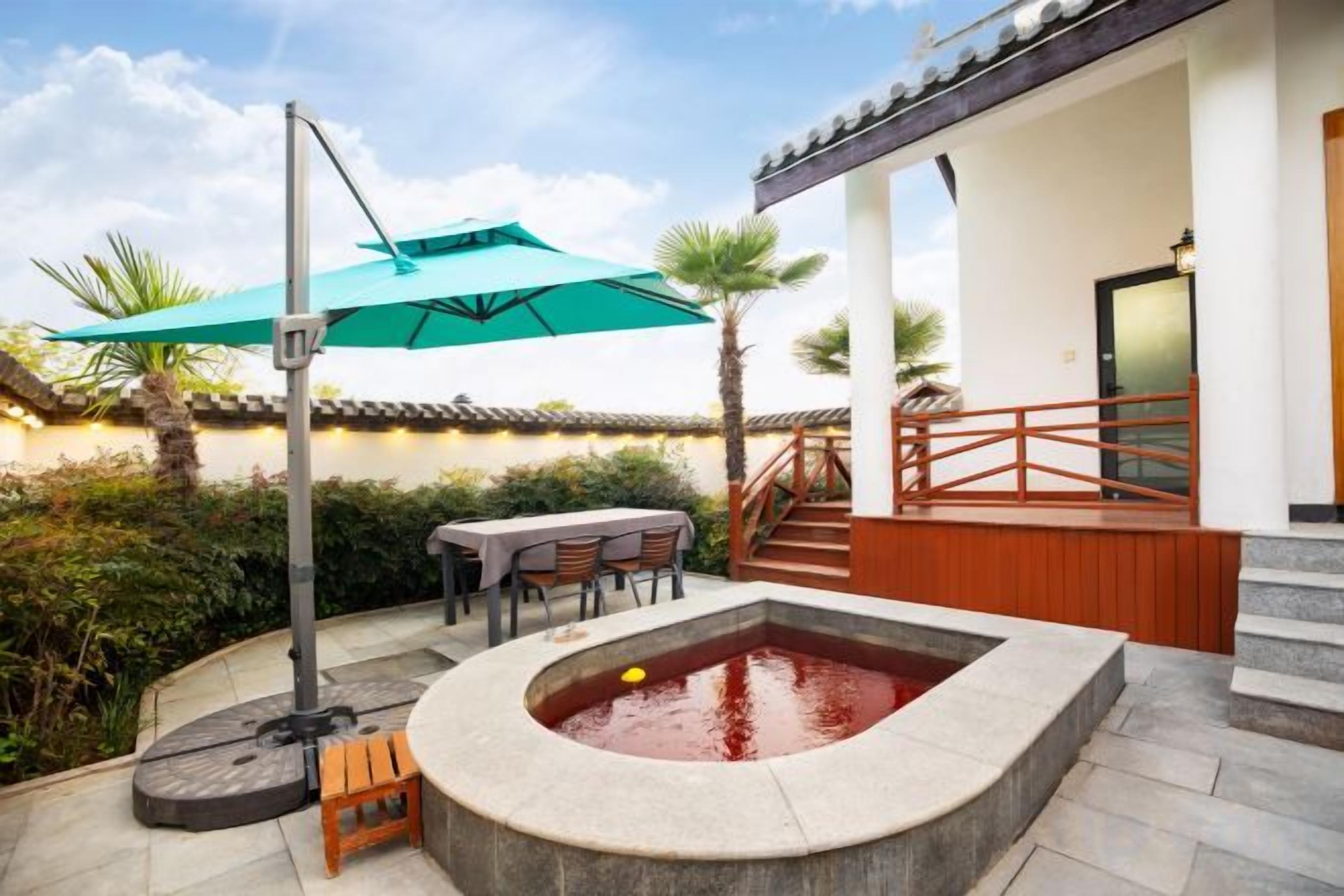 Ein Whirlpool in einem Innenhof mit einer Holzterrasse, Sitzgelegenheiten im Freien und einem überdachten Bereich mit Tisch und Stühlen.