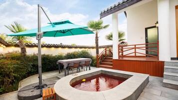 Ein Whirlpool in einem Innenhof mit einer Holzterrasse, Sitzgelegenheiten im Freien und einem überdachten Bereich mit Tisch und Stühlen.