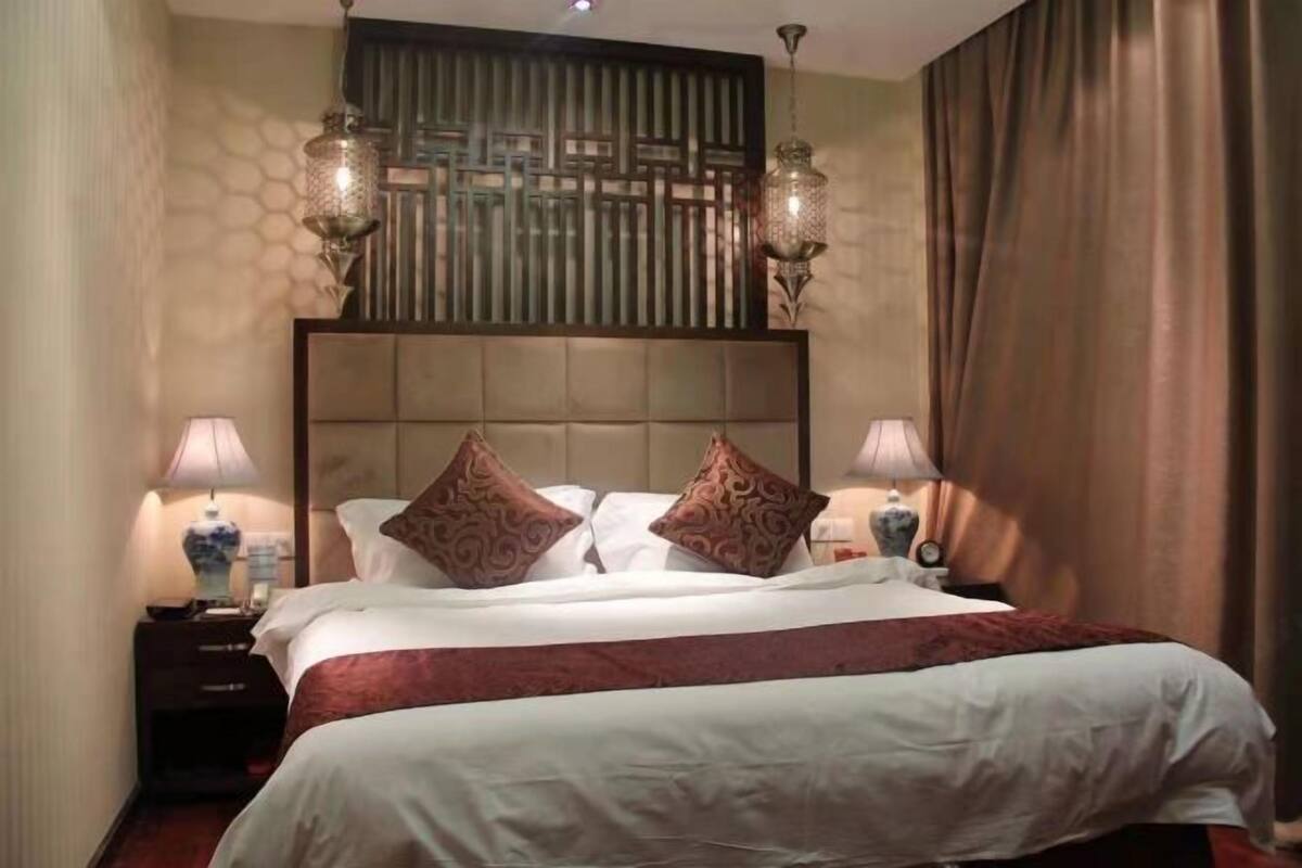 Habitación de hotel con una cama grande, dos mesitas de noche con lámparas, un panel decorativo en la pared y una cortina.