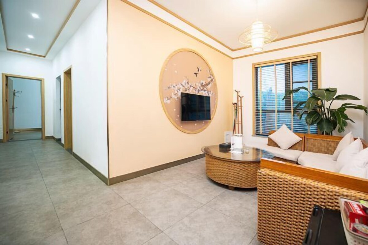 A hotel lobby with a reception desk, a large wall-mounted TV, a wicker sofa, and a potted plant.