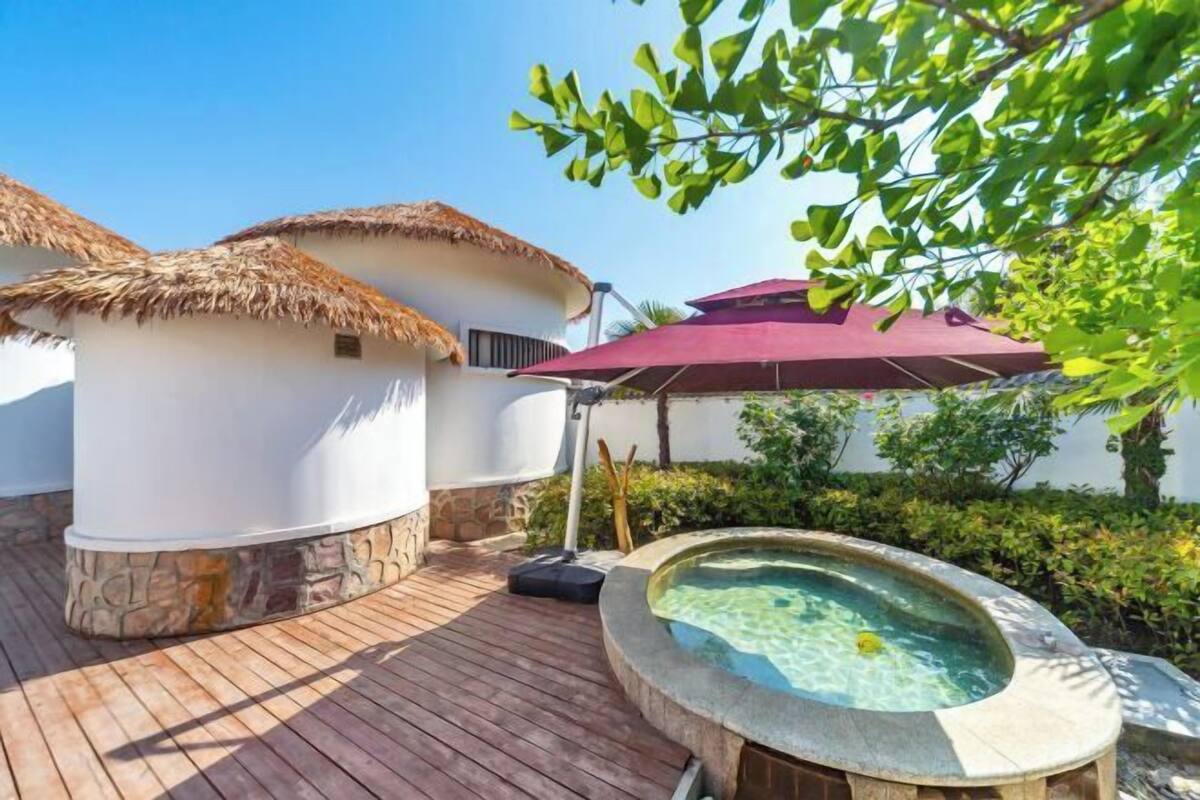 Un área de spa con una bañera de hidromasaje, construcciones de techo de paja y una terraza de madera.
