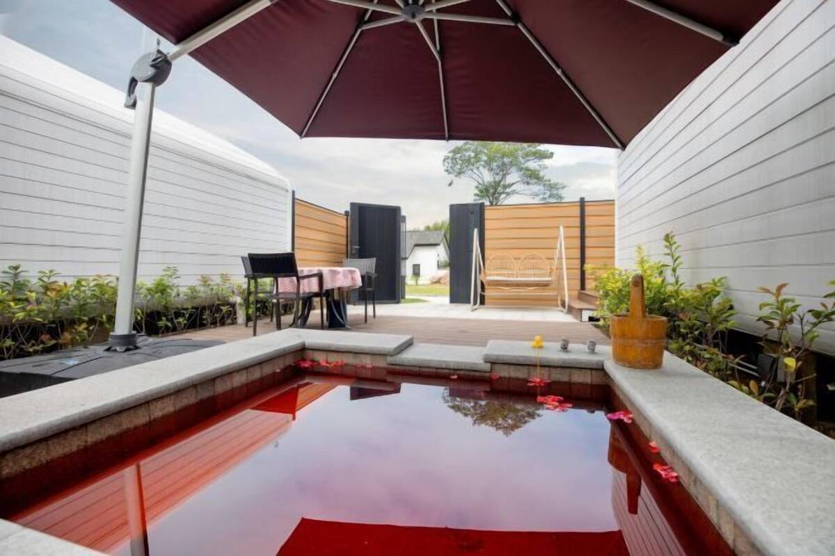 Una piscina con cubierta de madera, una mesa con sillas y un paraguas grande.