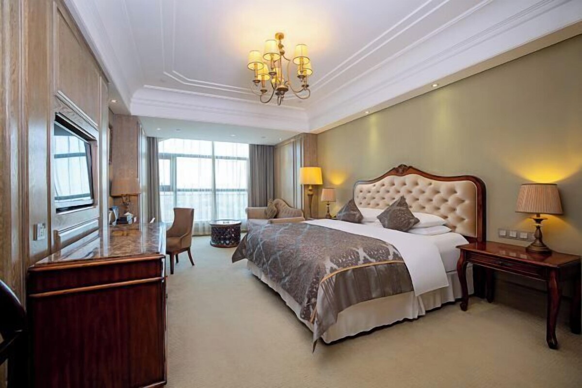 A hotel room with a large bed, a desk, a chair, and a chandelier.