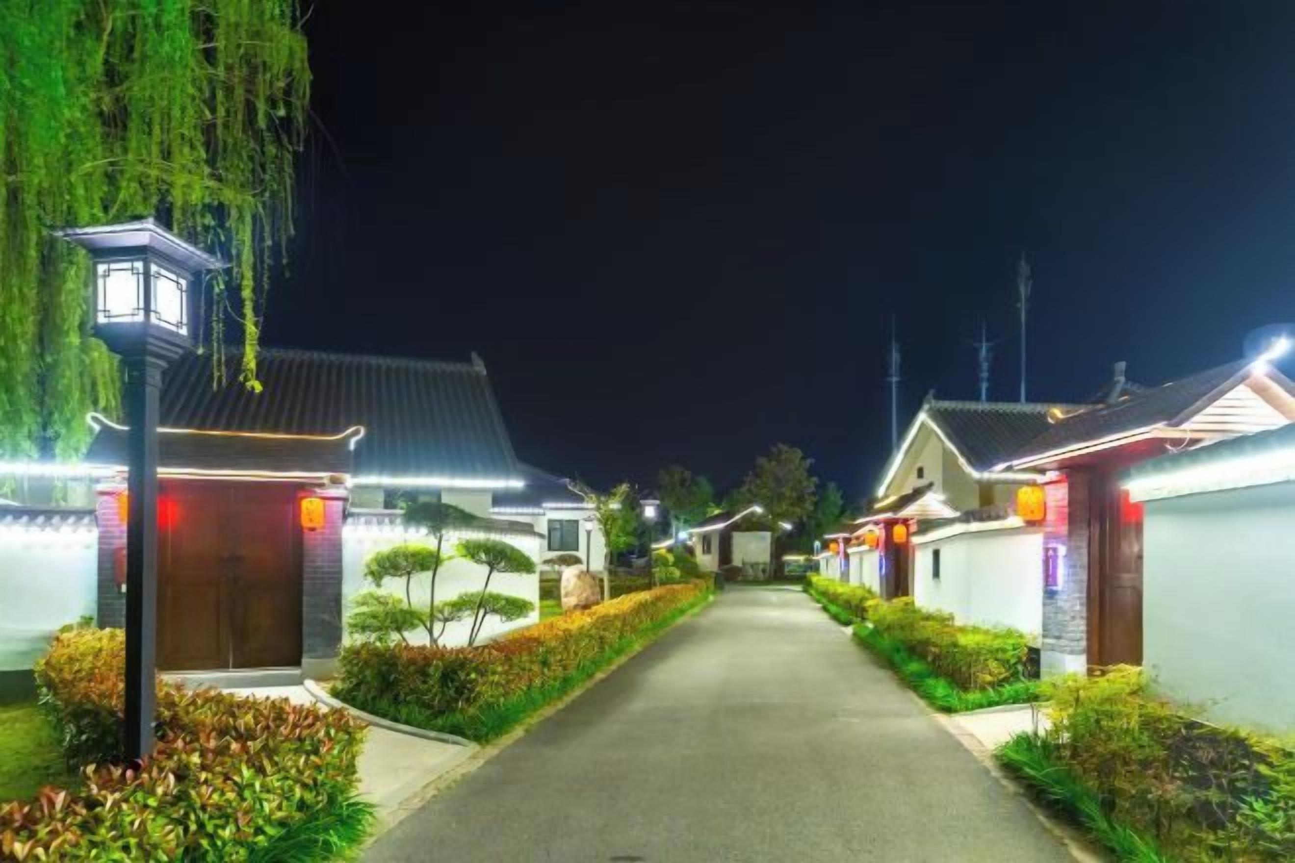 A pathway leading to traditional-style buildings with illuminated signage, surrounded by well-maintained hedges.