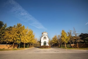 Una torre blanca con una cúpula y una entrada arqueada, rodeada de árboles y un camino pavimentado.