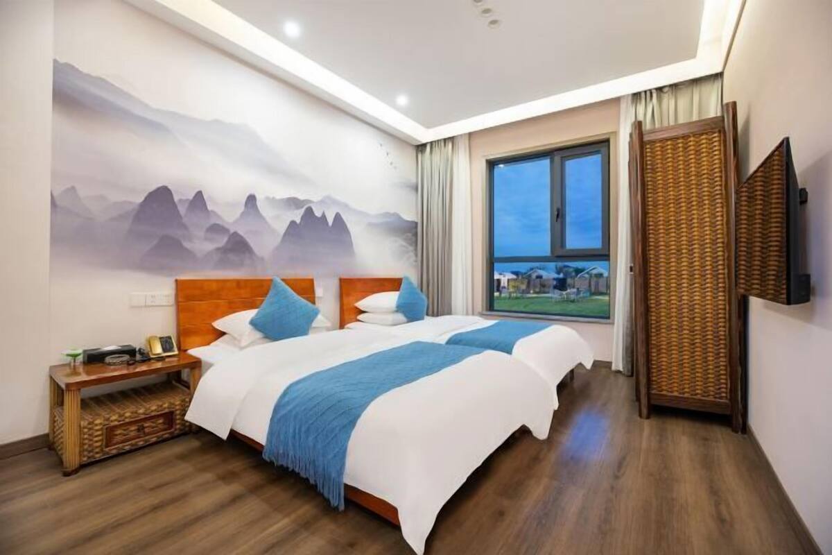 Habitación de hotel con una cama grande, una mesita de noche, un televisor y una ventana con vistas.
