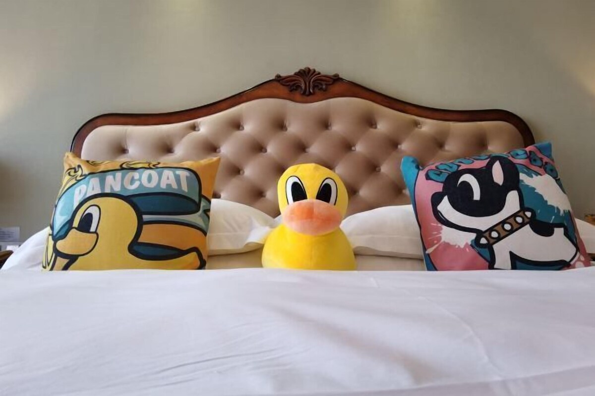 A bed with a tufted headboard, three pillows with cartoon characters, and a plush toy duck.