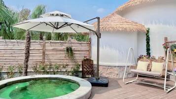 A pool with a white umbrella, a swing chair, and a thatched-roof structure.