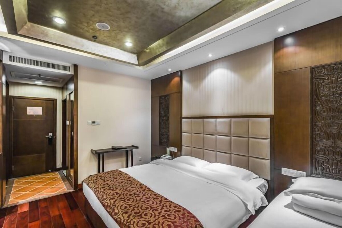 A hotel room with a large bed, a wooden headboard, a small bedside table, and a door with a mirror.