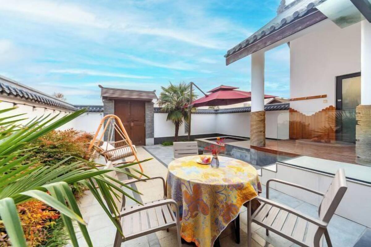 Un patio de estilo tradicional con una mesa redonda y sillas, una silla de madera y una palmera.