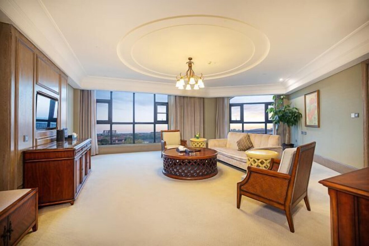 A spacious living room with a large window, a round coffee table, a sofa, and a wooden cabinet.