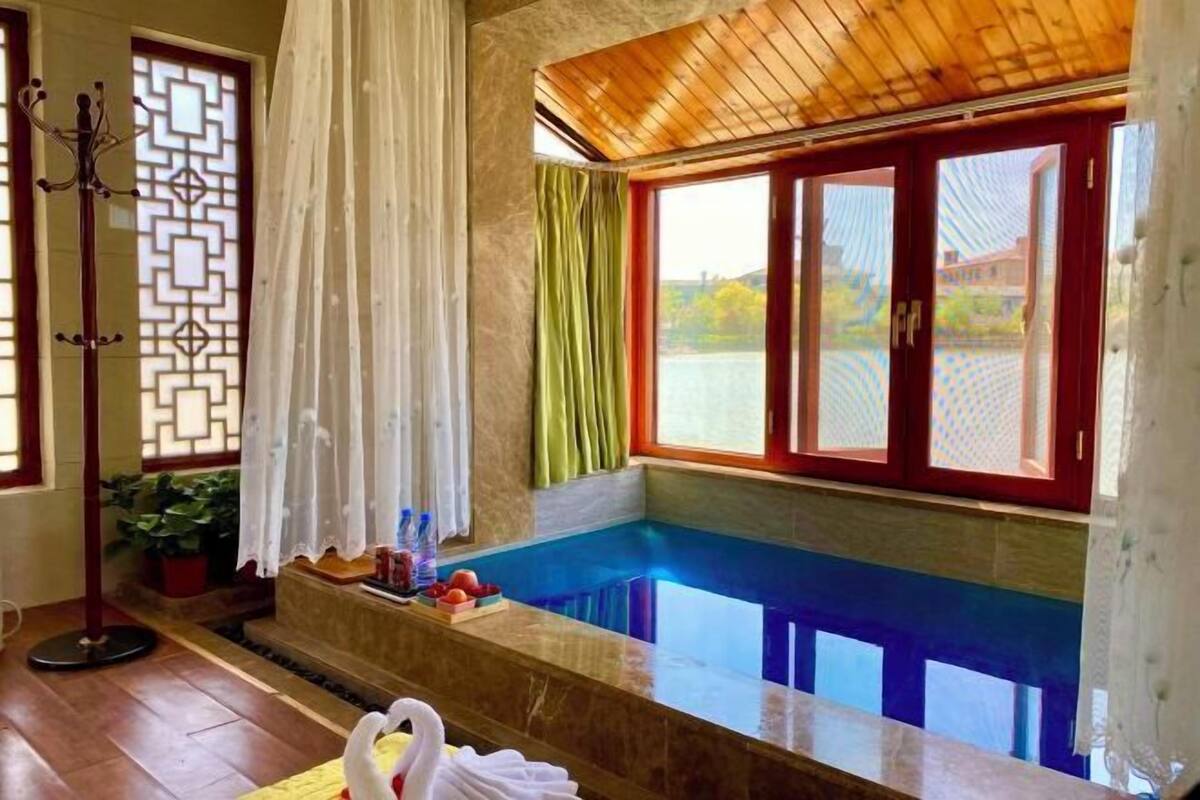 Una habitación con techo de madera, una ventana con marcos rojos, una bañera y una pequeña mesa con objetos encima.