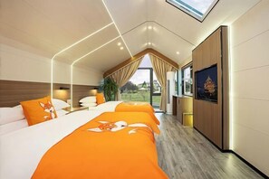 A hotel room with a sloped ceiling, two beds with orange bedding, a large window with curtains, and a framed picture on the wall. - Yanling Bloom Hot Spring Hotel (Yanling)