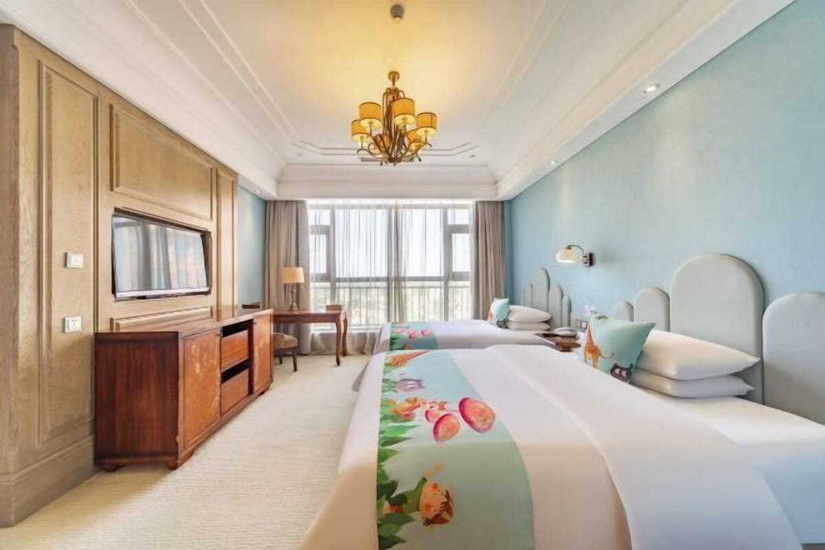 Habitación de hotel con una cama grande, televisión, escritorio y una araña.