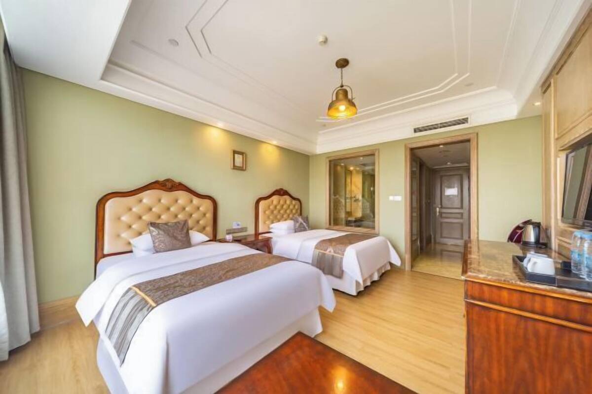 Habitación de hotel con dos camas, un aparador de madera, un espejo y una lámpara en el techo.