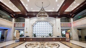 A spacious lobby with a central reception desk, a decorative floor pattern, and a large geometric wall design. - Yanling Bloom Hot Spring Hotel (Yanling)