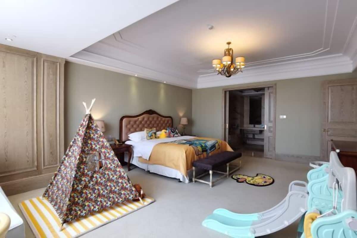 Una habitación de hotel con una cama, una tienda de campaña pequeña, un banco y una zona de juegos para niños.