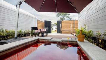A swimming pool with a red water feature, surrounded by a covered patio area with a table and chairs.