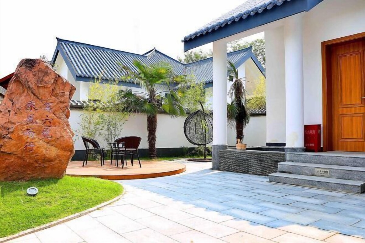 A traditional-style building with a tiled roof, a wooden door, and a stone pathway leading to a seating area with chairs and a table.