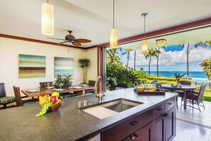 A modern kitchen with a large island, a dining area with a view of the ocean, and a ceiling fan. - Hale Papakea Ko Olina Beachfront Villa w/ Views (Kapolei)