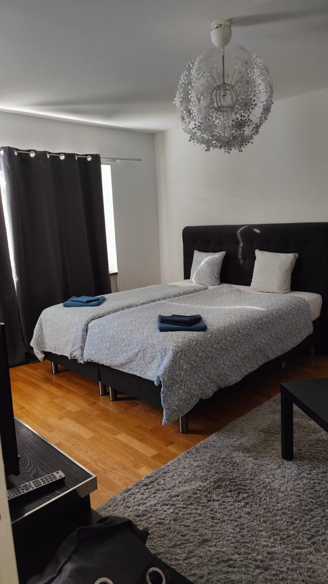 A modern bedroom with a large bed, a chandelier, and a wooden floor.