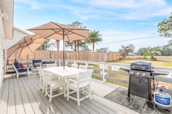A deck with a white table and chairs, a barbecue grill, and two large umbrellas. - Bowline Bungalow Tybee Vacation Rentals (Tybee Island)