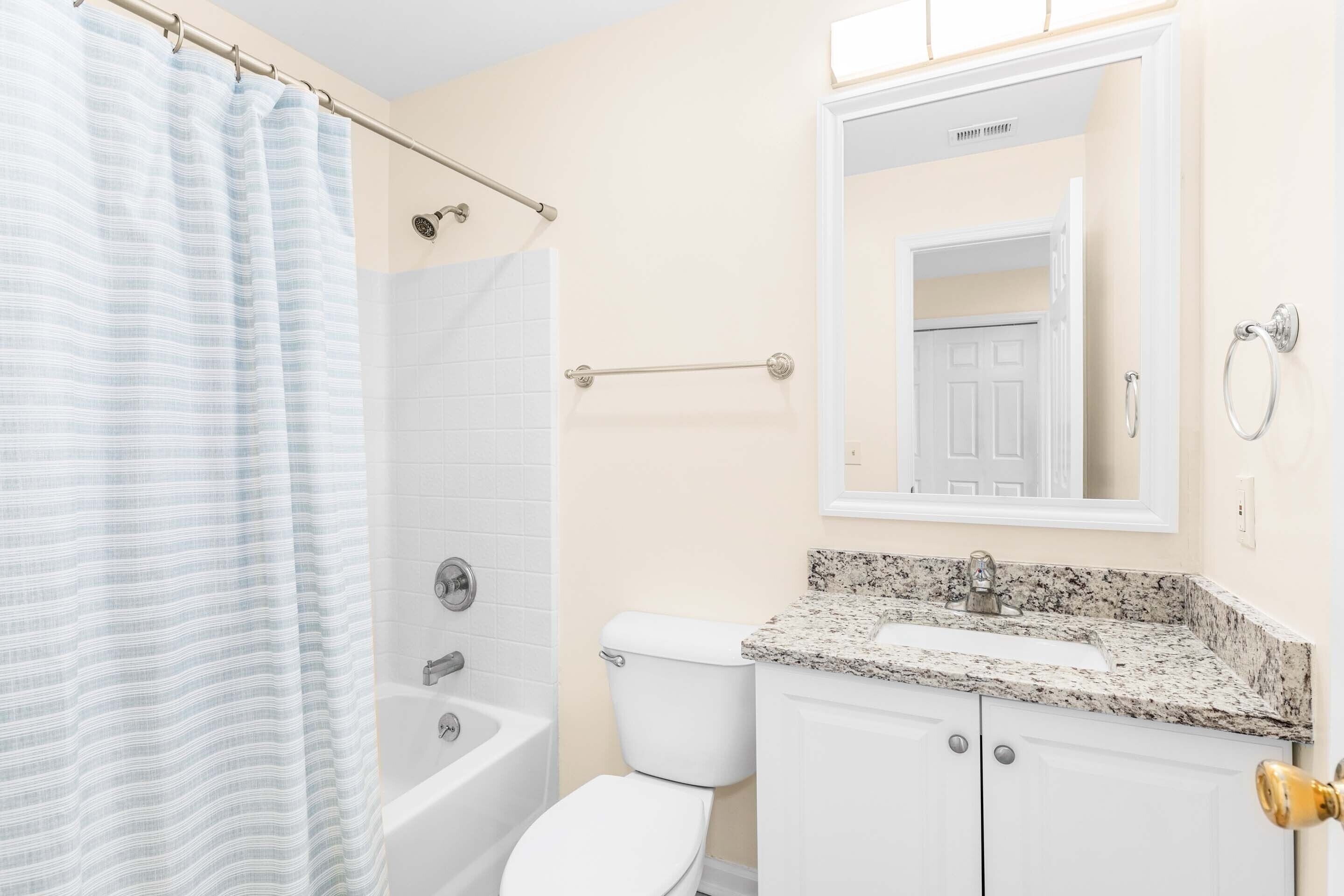 A bathroom with a shower, toilet, sink, and a mirror above the sink.
