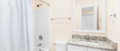 A bathroom with a shower, toilet, sink, and a mirror above the sink.